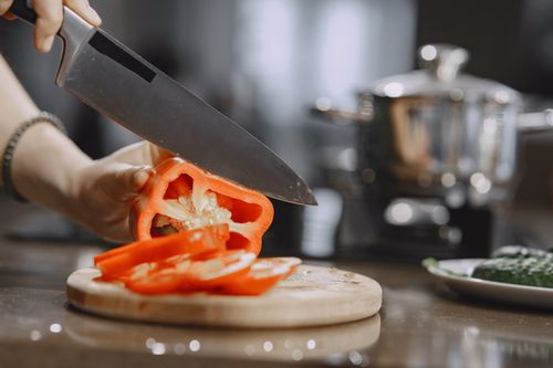 Free Close-up of slicing fresh red bell pepper on wooden board in modern kitchen. Stock Photo