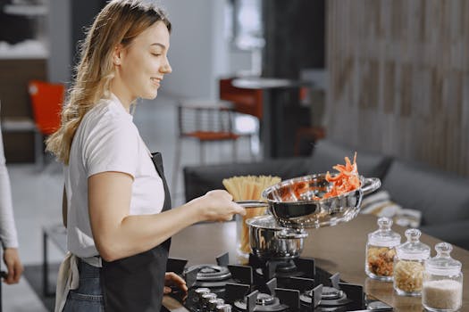 A woman in an apron cooking pasta with fresh vegetables in a modern kitchen.