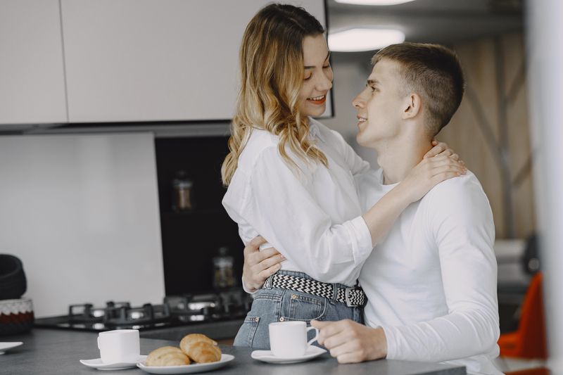 A young couple shares a tender moment in a modern kitchen, enjoying coffee together.