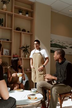 A diverse group of adults enjoying coffee and conversation with a friendly barista in a modern cafe setting.