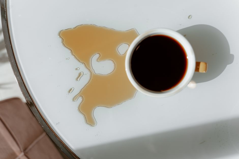 自然光の中、白いテーブルの上にあるコーヒーカップとこぼれたコーヒーの俯瞰視.