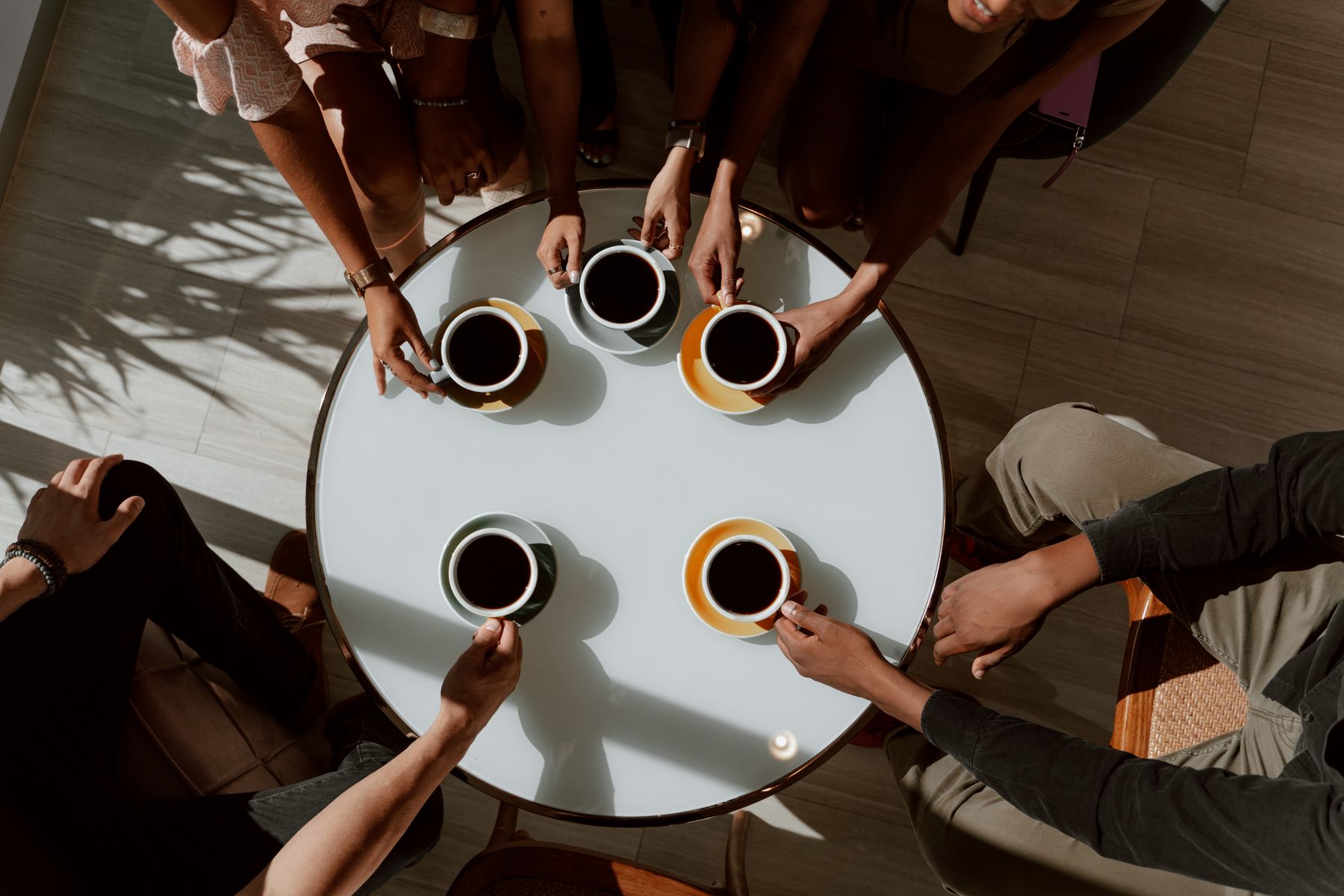 Overhead view of friends around a round cafe table with cups of coffee — photo by RDNE Stock project on Pexels