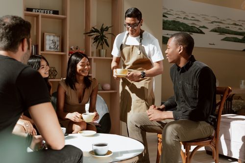 Free A group of friends enjoying coffee served by a waiter in a cozy café setting. Stock Photo