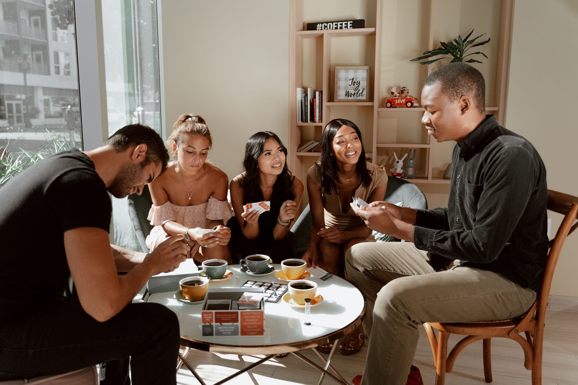 Group of diverse friends playing board games in a cozy café setting, enjoying coffee together.
