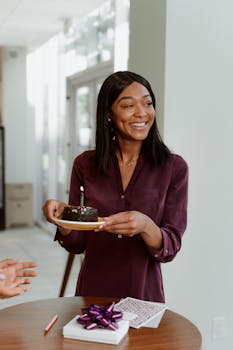 Woman celebrating birthday indoors with a chocolate cake, exuding happiness.