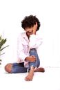 Trendy ethnic man in ripped jeans with Afro hairstyle looking at camera while sitting with crossed legs on white background