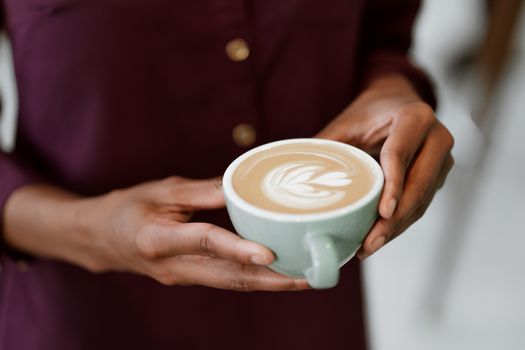 A detailed view of a person's hands holding a ceramic cup featuring beautiful latte art on top.. pexels, detailed, view