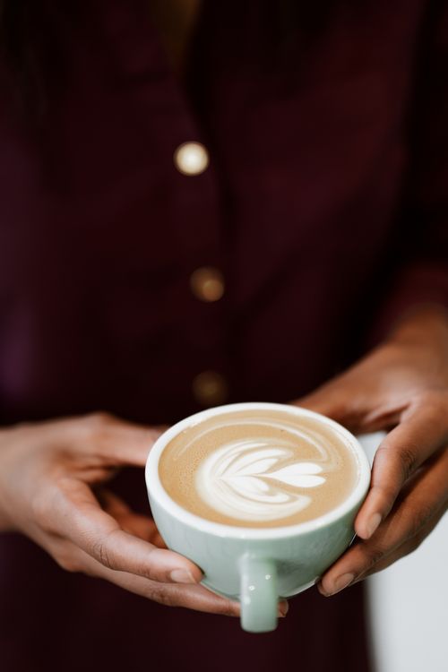 Free Close-up of a person holding a ceramic cup with intricate latte art, showcasing frothy coffee perfection. Stock Photo