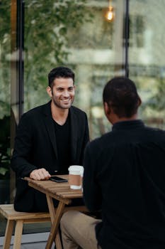 Two men having a cheerful conversation over coffee at an outdoor cafe table.
