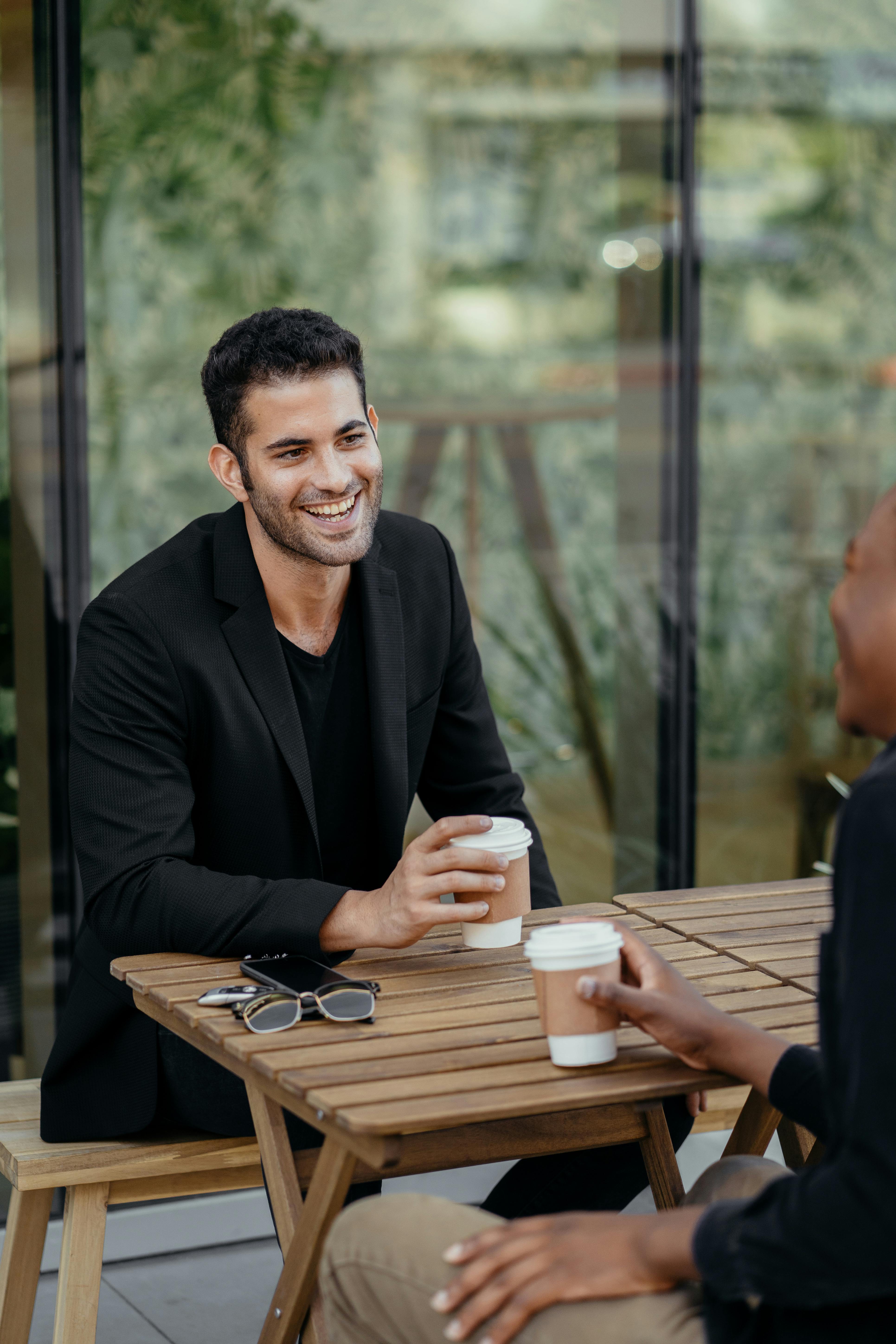 两名男子在户外咖啡馆的餐桌上，一边享用咖啡一边交谈，营造出休闲而专业的氛围