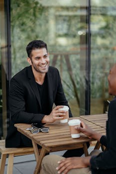Two men enjoying coffee and conversation at an outdoor café table, creating a casual yet professional atmosphere.