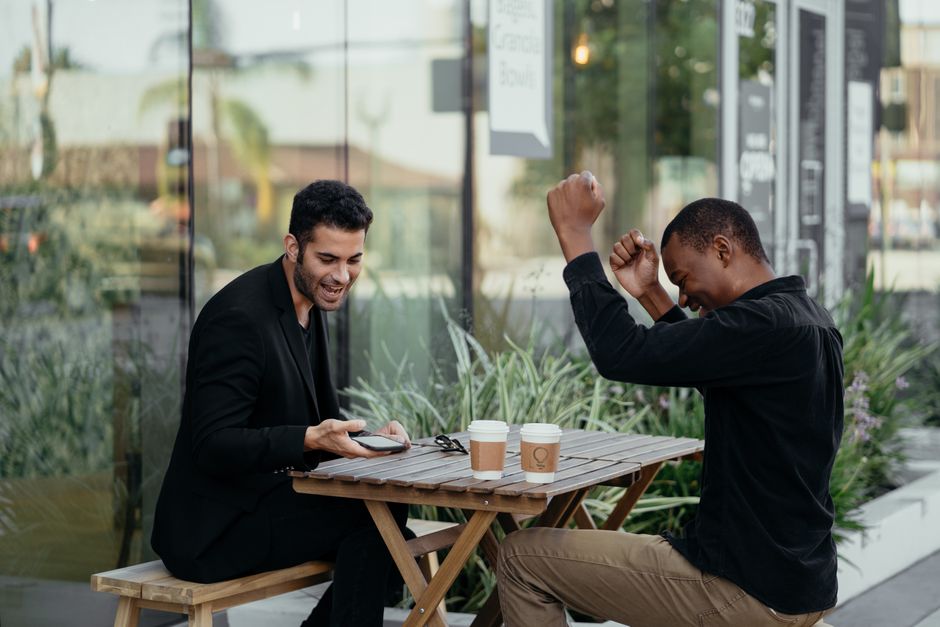 Two colleagues rejoice over successful news while enjoying coffee outside a café. Two colleagues rejoice over successful news while enjoying coffee outside a café.