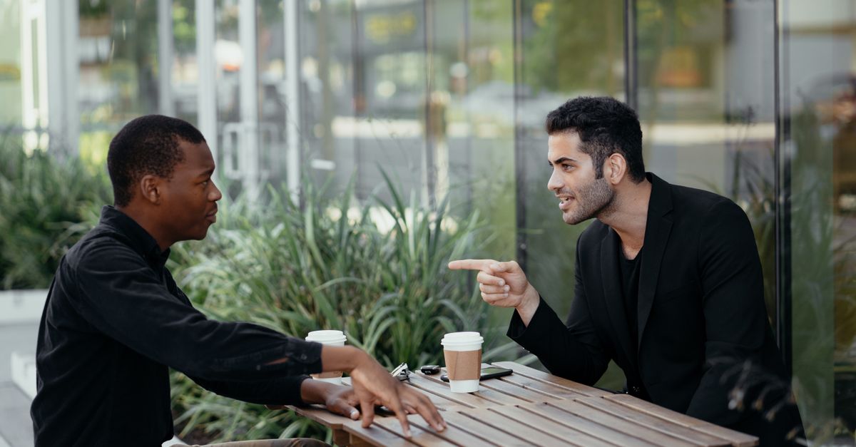 Two men seated at an outdoor café having a lively conversation over coffee.