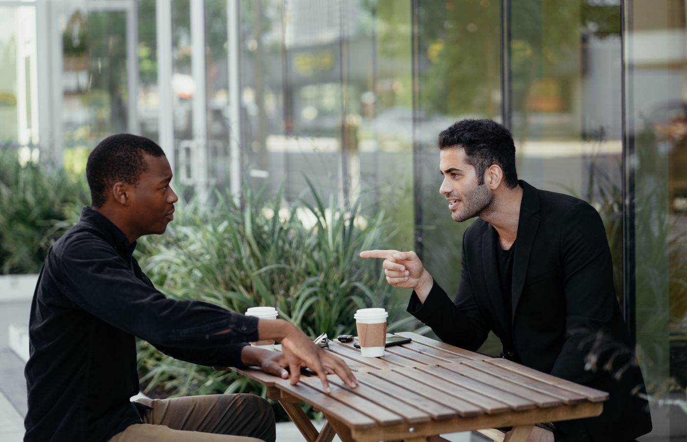 Two men seated at an outdoor café having a lively conversation over coffee.