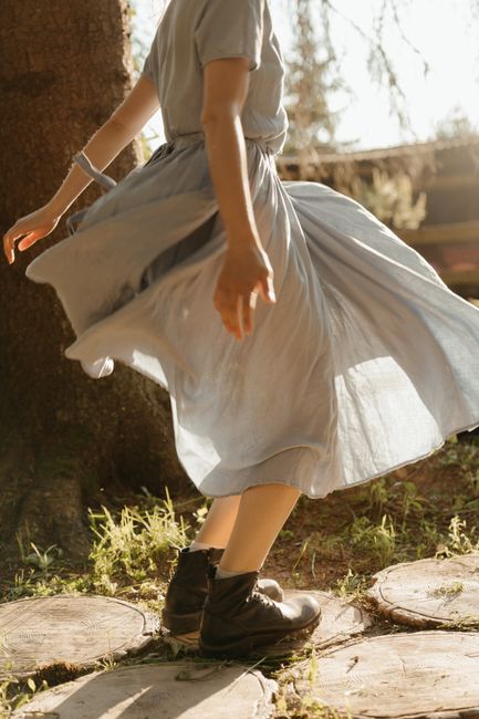 A woman in a flowing dress dances outdoors on rustic stepping stones.