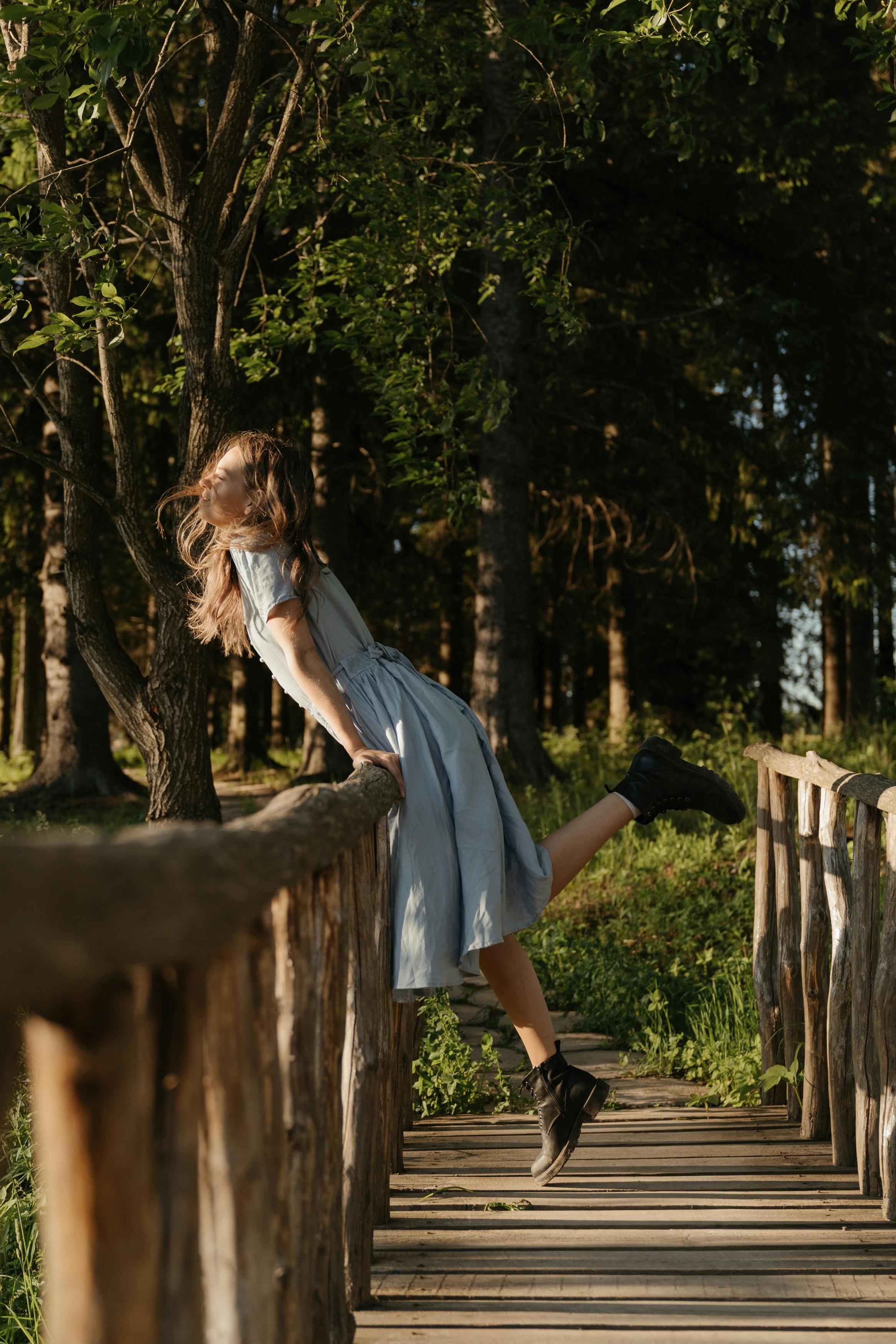 一个无忧无虑的年轻女子在一个蓝色的衣服靠在一个阳光明媚的森林设置木桥