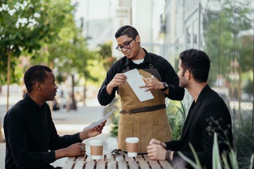 Free Casual outdoor meeting at a café with diverse friends and friendly waiter. Stock Photo