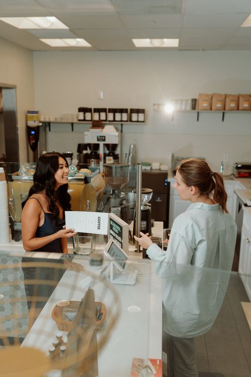 Free A barista serves a smiling customer at a modern coffee shop counter with a clear menu visible. Stock Photo