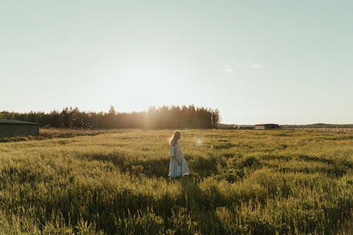Woman in White Dress Walking on Green Grass Field