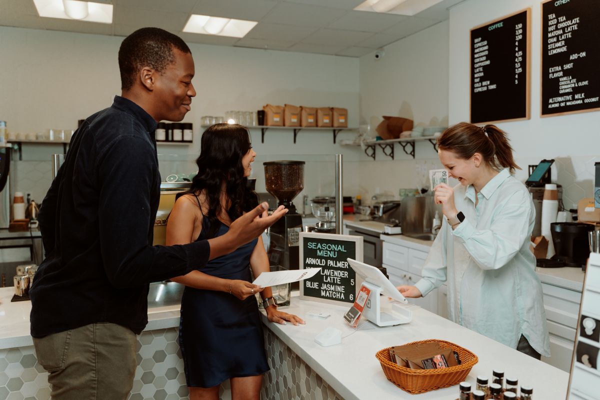 A barista chatting with two smiling customers at a modern café counter