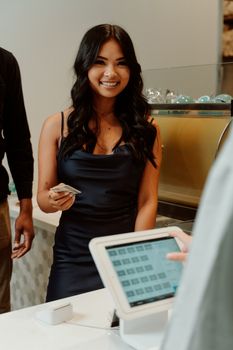 一名身穿黑色连衣裙的女子在商店无现金付款时微笑着