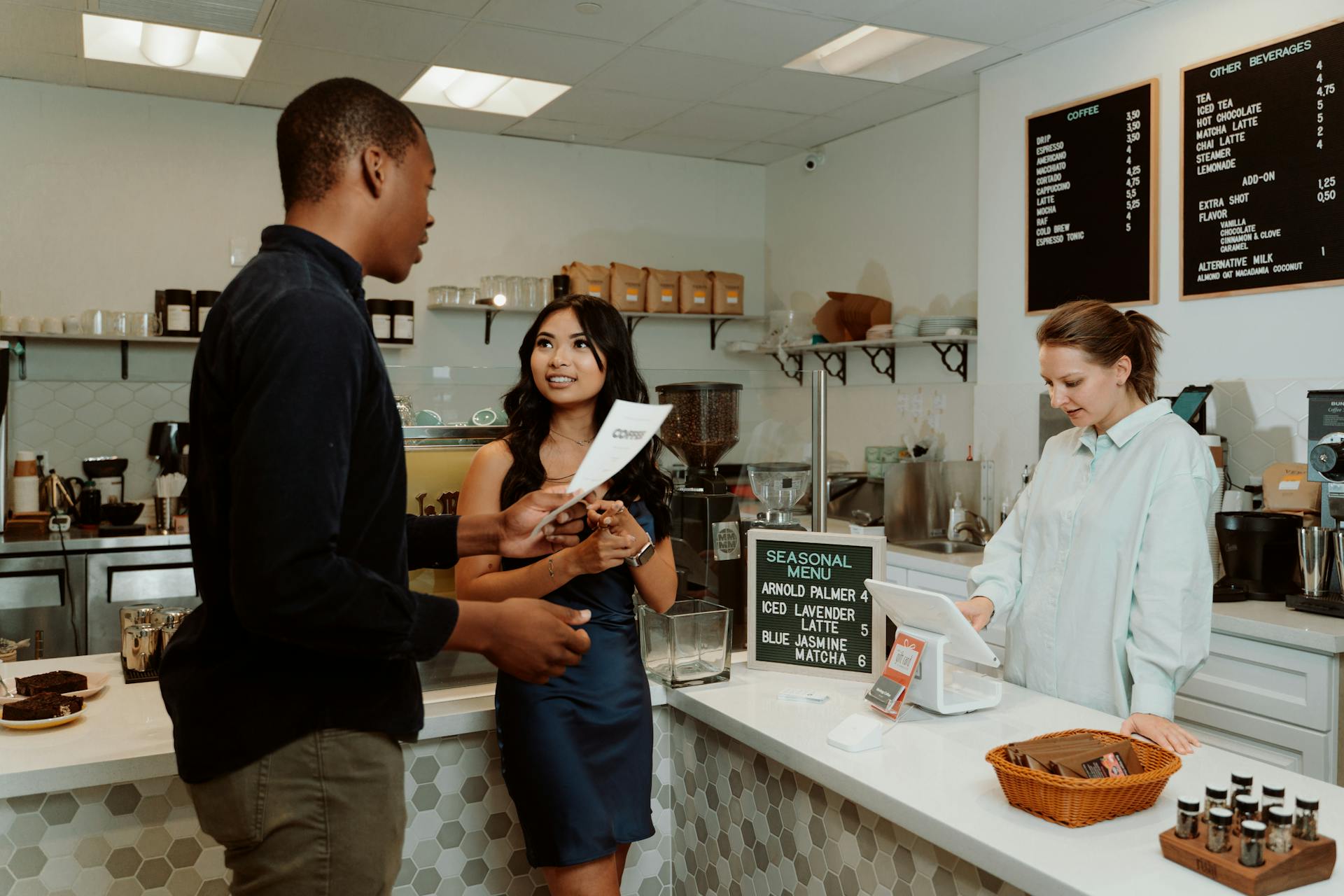 Two customers engage with a barista while ordering at a modern café counter.