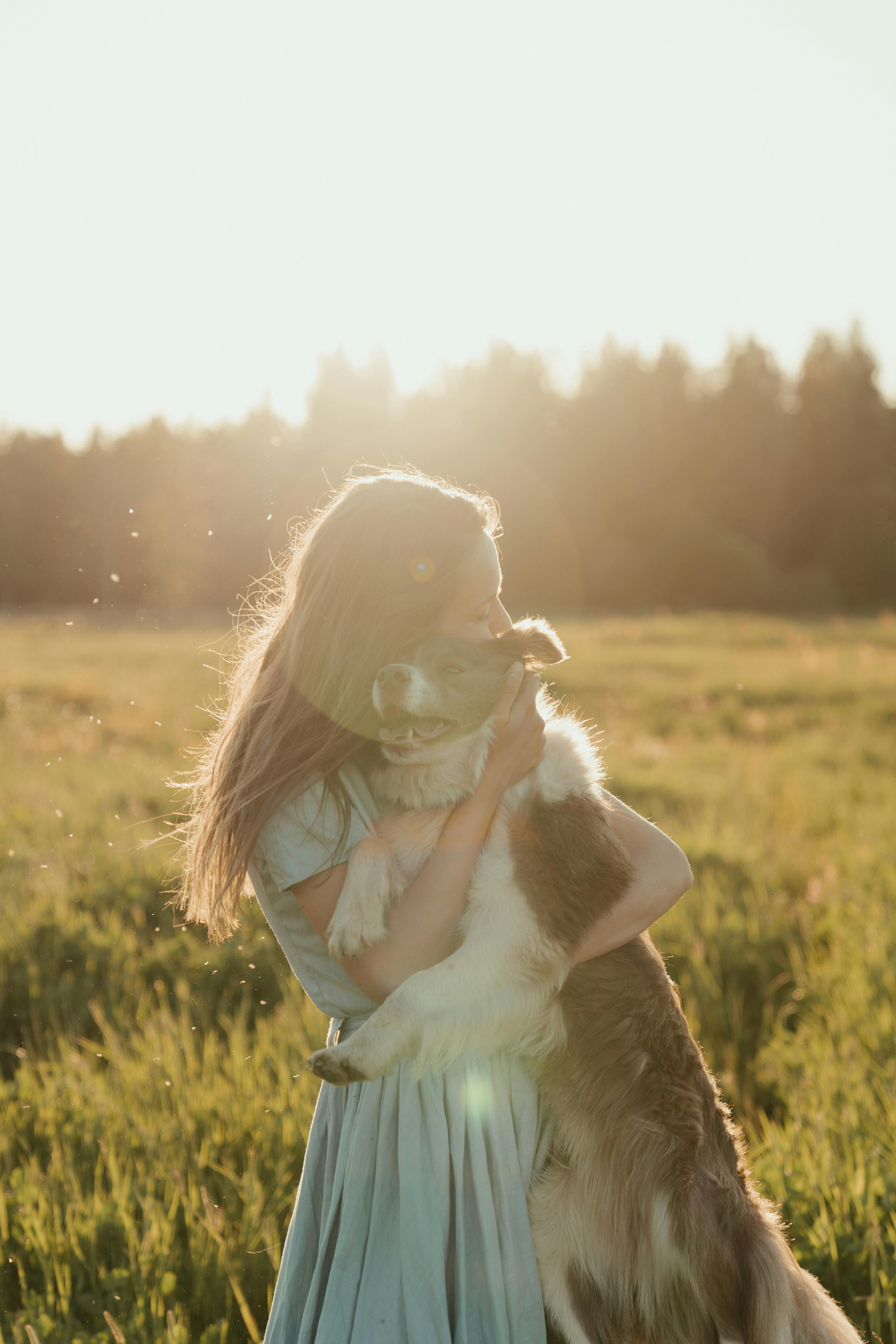 girl in white long sleeve shirt holding white and brown short coated dog on green grass