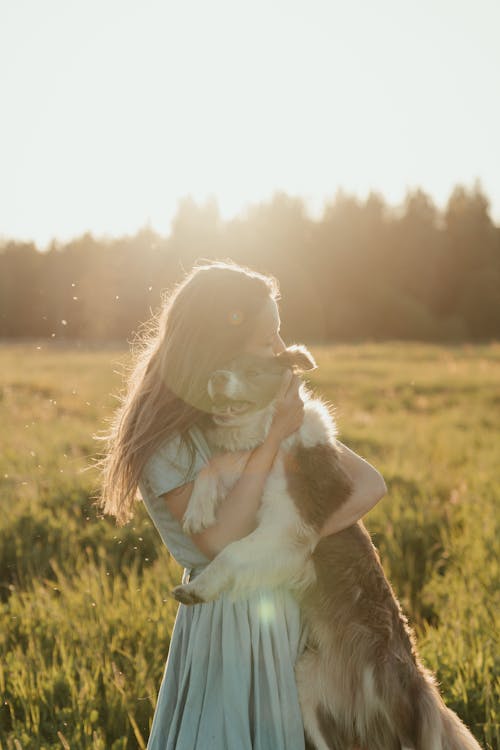 Girl in White Long Sleeve Shirt Holding White and Brown Short Coated Dog on Green Grass