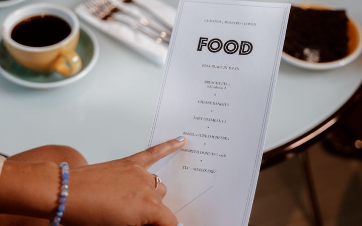 Close-up of hands selecting food options from a menu in a cozy café setting.
