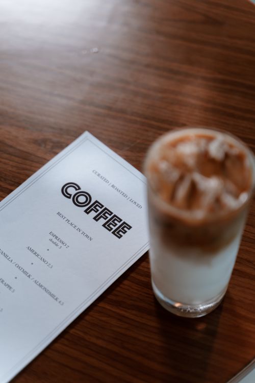 Free Iced coffee placed on a wooden table beside a menu, offering a cozy cafe vibe. Stock Photo