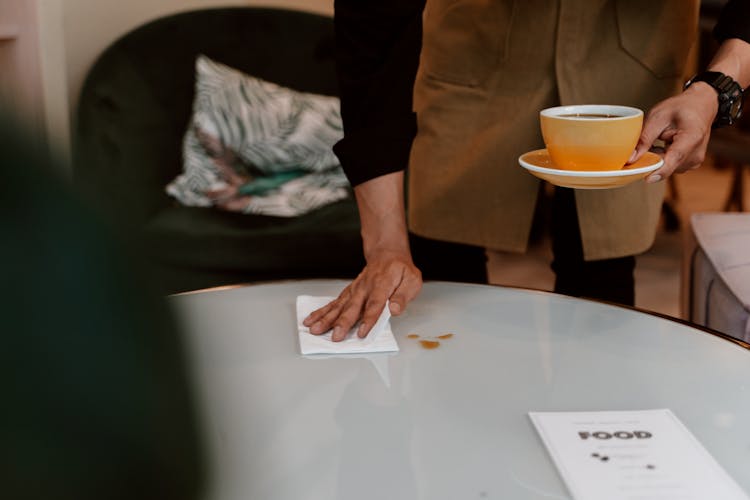 Waiter Cleaning Table Top While Holding A Ceramic Cup 