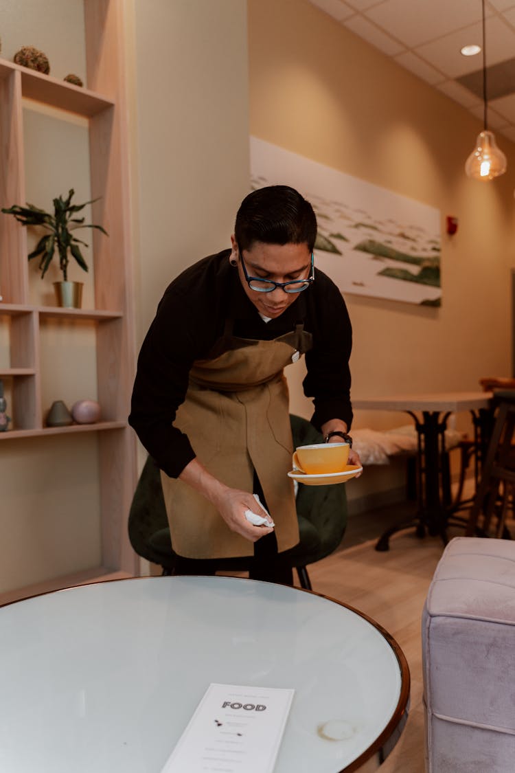 Waiter Cleaning Table Top While Holding A Ceramic Cup