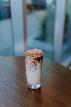 A glass of iced coffee with milk swirls on a wooden table indoors.