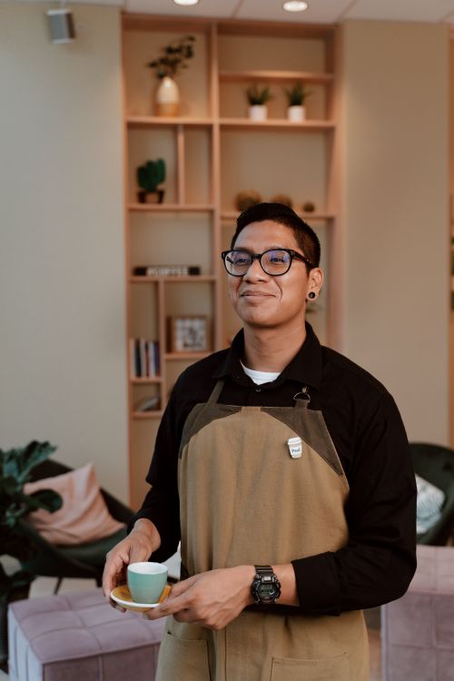Free Confident barista smiling while holding a coffee cup in a cozy cafe setting. Stock Photo