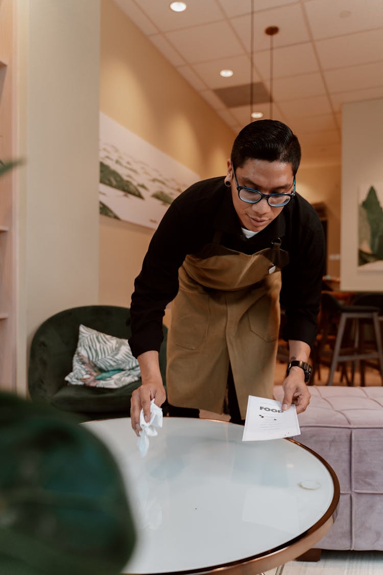 Waiter Cleaning Table Top While Holding A Paper