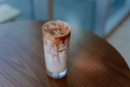 A refreshing glass of iced coffee with milk on a wooden table with a blurred background.