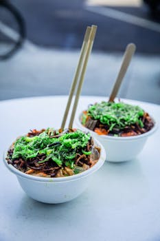 Vibrant Asian cuisine bowls topped with greens and chopsticks on a white table.