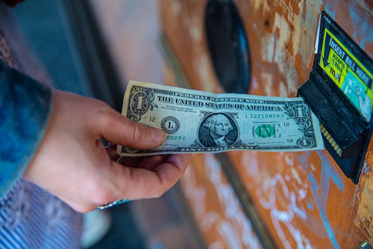 A Person Inserting A Dollar Bill In A Machine