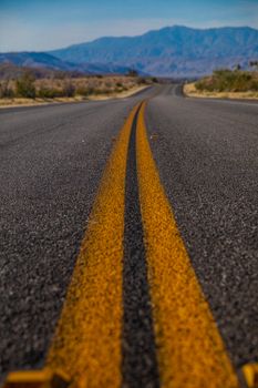 一条黄线鲜艳的废弃道路，在晴朗的天空下一直延伸到远处的山脉