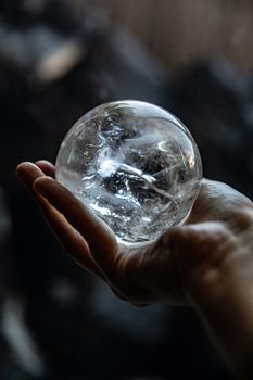一只手握着一颗透明水晶球，在变幻莫测的黑暗背景中反射着光线
