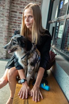 在城市地区，一名白人妇女和一只边境牧羊犬坐在靠砖墙的木凳上