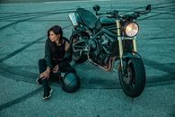 A Woman in Black Jacket and Black Pants Sitting Beside a Black Motorcycle