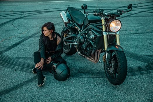 A Woman in Black Jacket and Black Pants Sitting Beside a Black Motorcycle