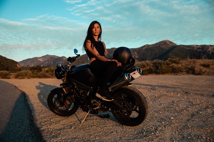 Woman In Black Tank Top Riding On Black Motorbike Near The Road