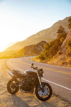 A sleek motorbike parked along a winding mountain road during a picturesque sunset.