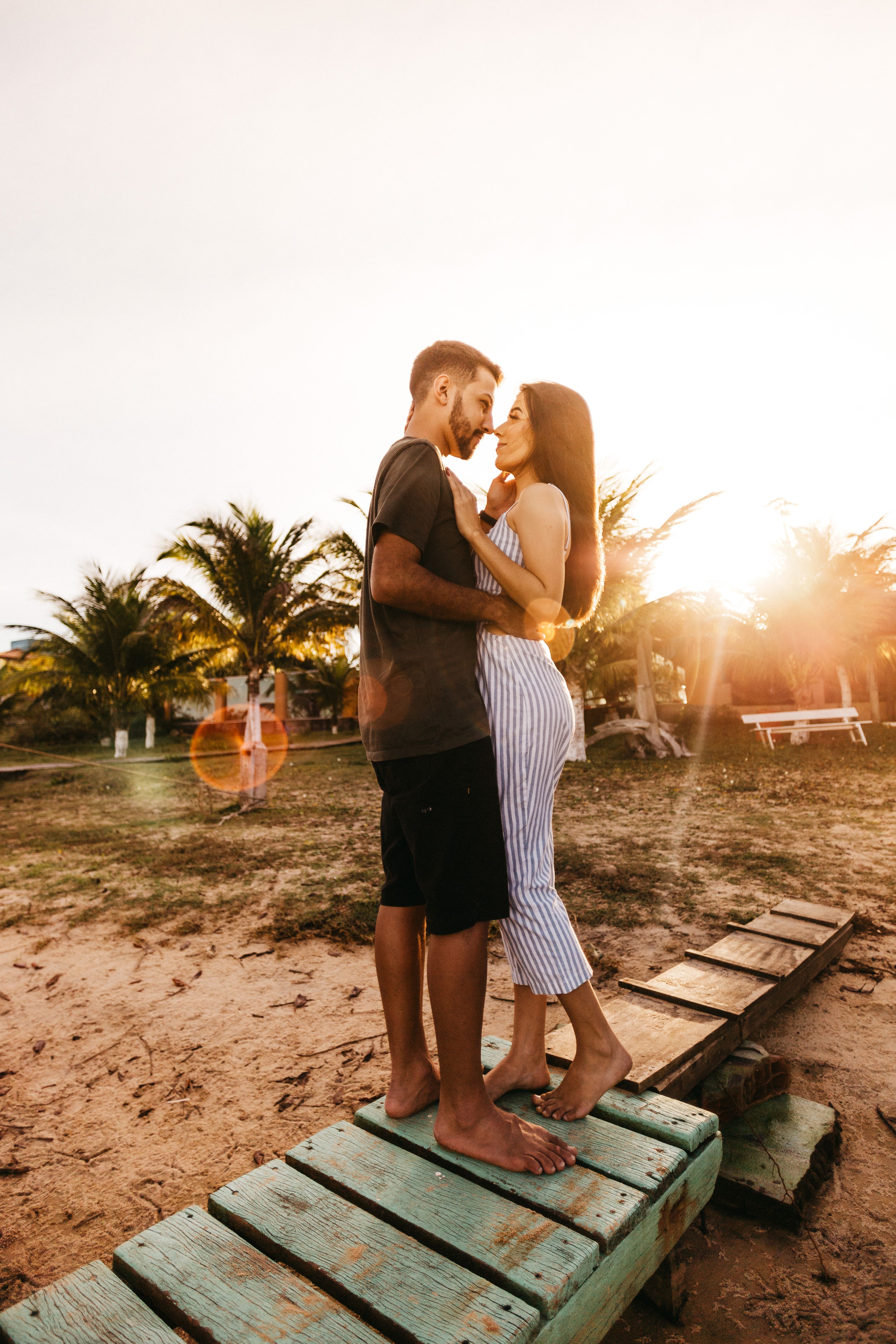 Side view full length barefoot couple in stylish summer wear standing on tropical beach and embracing gently while looking at each other