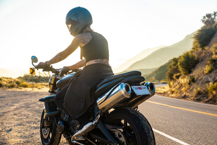 Tattooed Woman In Black Helmet Sitting On A Motorcycle By The Road