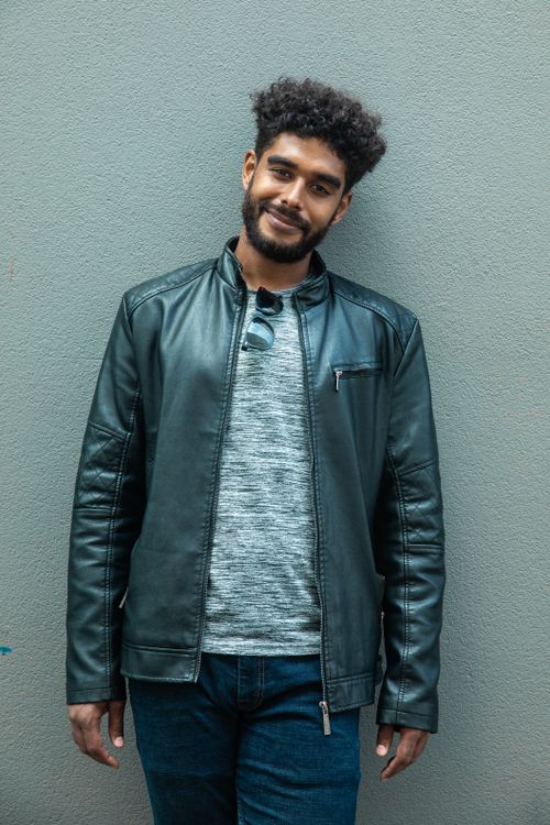 Free Confident young man in a leather jacket poses against a neutral wall, showcasing modern fashion. Stock Photo