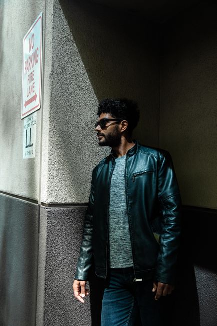 Portrait of a man in a leather jacket and sunglasses standing next to a no parking sign.