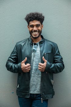 自信的年轻人穿着黑色皮夹克，微笑着竖起大拇指